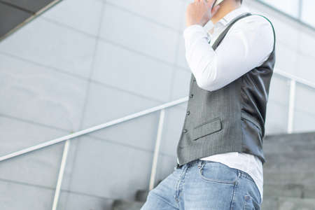 Young and Casual Businessman Using Smartphone while Walking Outside of Office Buildingの写真素材