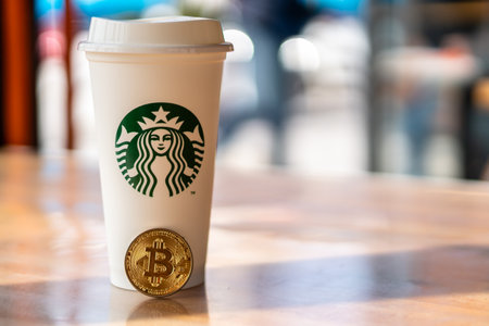Cryptocurrency Bitcoin next to Starbucks cup. Starbucks adoption of blockchain concept - Slovenia - 28.2.2019のeditorial素材