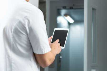 Bright close up of male doctor in uniform with stethoscope and using computer tablet in hospital. Modern medical conceptの写真素材