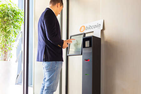 Bitcoin ATM machine being used by businessman for buying cryptocurrency and other altcoinsの写真素材