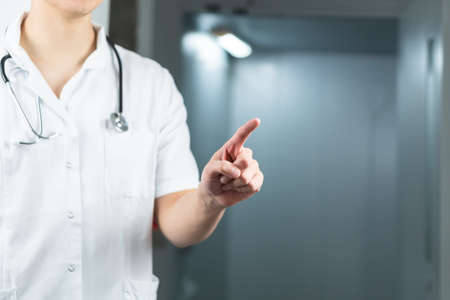 Bright close up of male doctor in uniform with stethoscope pointing finger in the air. Copy space or graphic spaceの写真素材