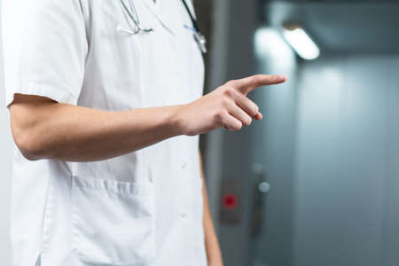 Bright close up of male doctor in uniform with stethoscope pointing finger in the air. Copy space or graphic spaceの写真素材