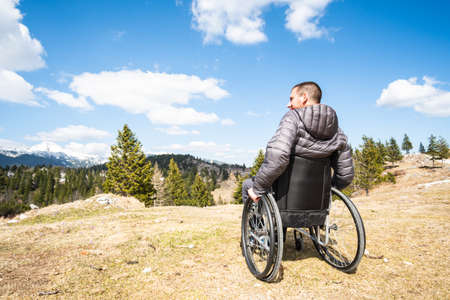 Wide angle photo ofYoung disabled man in wheelchair outside in nature observing mountains and natureの写真素材