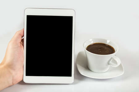 Digital tablet in one hand, on a white background next to coffee mug full of coffee, isolatedの写真素材