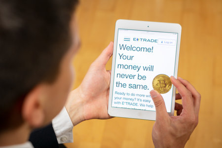 ETrade website on a tablet and businessman trader holding Bitcoin.
