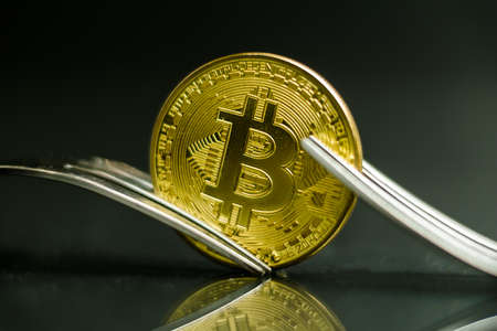 Bitcoin cryptocurreny coin placed between forks with reflection, hard forkの写真素材