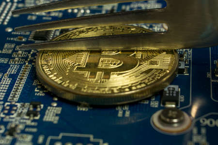 A single Bitcoin coin on the blue computer motherboard and fork trying to half it
