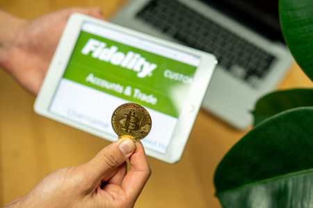 Ljubljana, Slovenia 29.4.2019: Businessman holding computer tablet with opened Fidelity website and Bitcoin coin on a office deskのeditorial素材