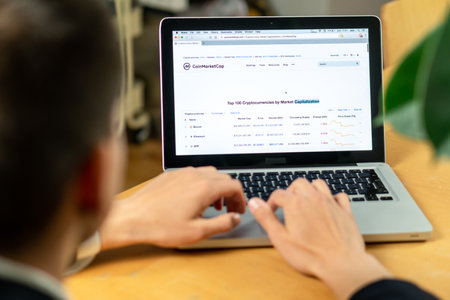 Ljubljana, Slovenia 29.4.2019: businessman sitting at office desk front laptop computers with financial graphs and statistics on monitor website.のeditorial素材