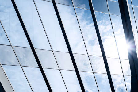 closeup of a modern window glass building with sun and blue sky reflecting in itの写真素材