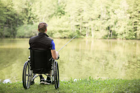 Happy and young disabled or handicapped man fishing at a lake in nature. Popular sport for paraplegics.の写真素材