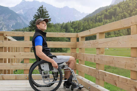 Disabled young man on a wheelchair on a wooden bridge path enjoying in nature looking at beautiful viewの写真素材