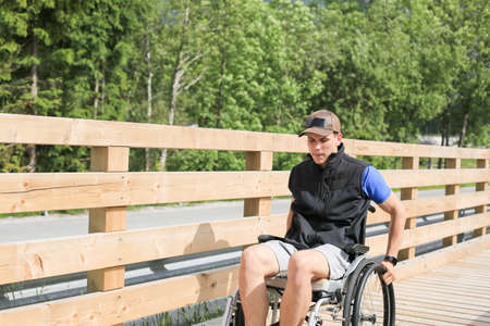 Disabled young man on a wheelchair on a wooden bridge path enjoying in nature