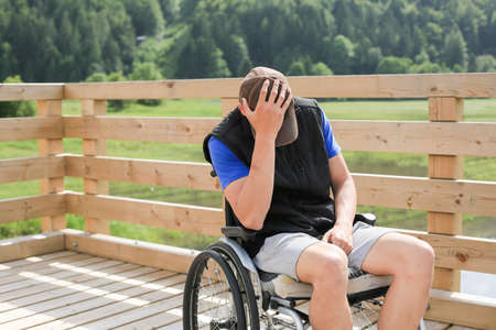 Disabled young man on a wheelchair in nature feeling depressed, lonely and sadの写真素材