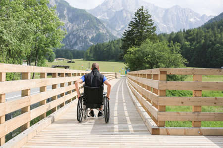 Disabled young man on a wheelchair on a wooden bridge path enjoying in natureの写真素材