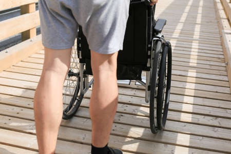 Assistant pushing wheelchair outside in nature on a wooden bridge pathの写真素材