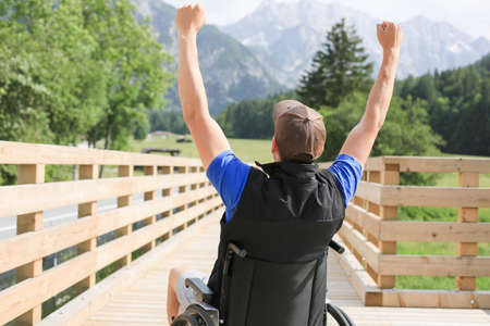 Disabled young man on a wheelchair in nature feeling excited and full of optimism like a winnerの写真素材