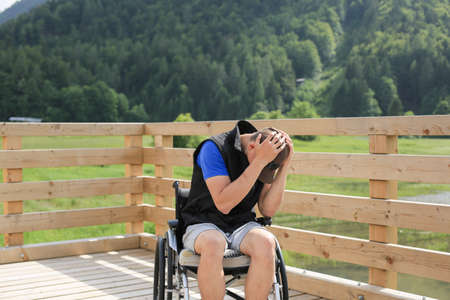 Disabled young man on a wheelchair in nature feeling depressed, lonely and sadの写真素材
