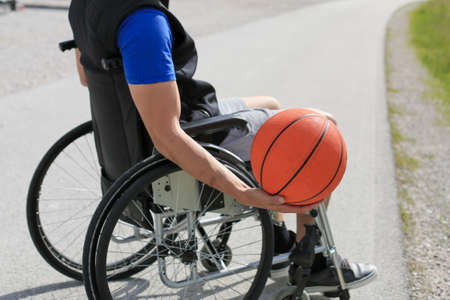 Disabled young basketball player on a wheelchair holding ball and beeing active in sportの写真素材