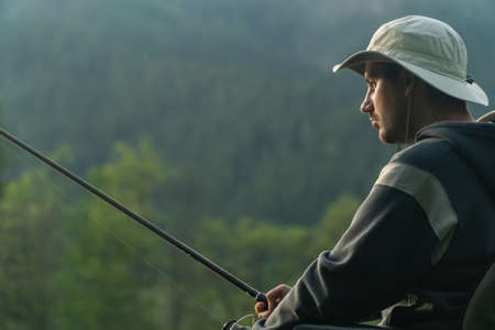 young man in a wheelchair fishing at the beautiful lake in sunset, dawnの写真素材