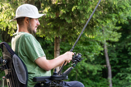 Happy man in a electric wheelchair fishing at the beautiful pond in natue on a sunny dayの写真素材
