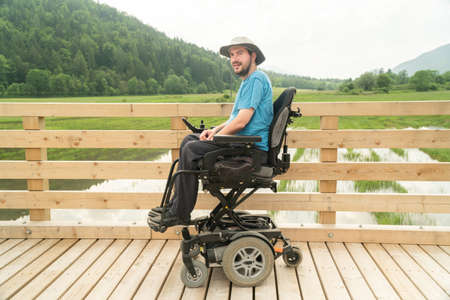 disabled happy young man in electric wheelchair on a boardwalk enjoying his freedom and smiling