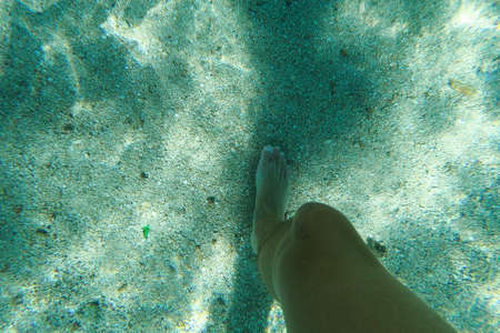 Legs walking on beach perfect white sand turquoise water, reflecting from sun. Underwater photo