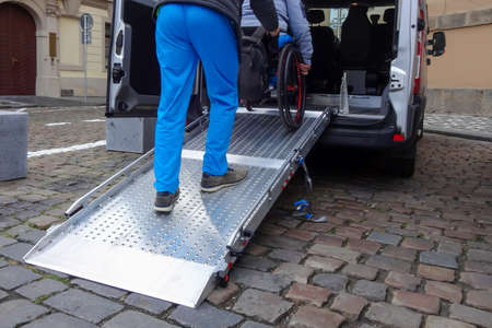 Assistant helping disabled person on wheelchair with transport using accessible van rampの写真素材