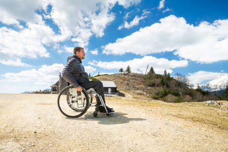 Happy man in wheelchair outside in nature on a sunny summer day in the mountains