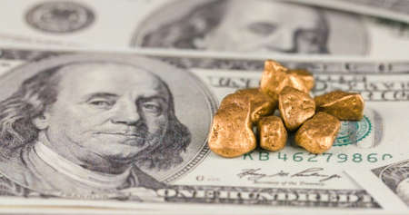 Gold nuggets pile lying on the hundred american dollar usd money bills