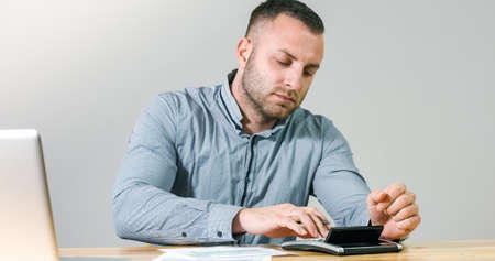 Frustrated businessman under stress nervously filling 1040 tax form with calculator at office desk.