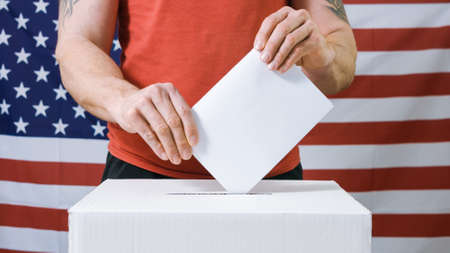 Young man voting and casting ballot in a box at flag of USA