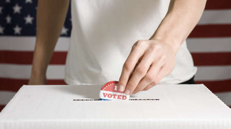 Young man casting I Voted Today Button in a box at flag of USAの写真素材