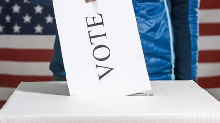 Woman voting and casting ballot in a box at flag of USA.