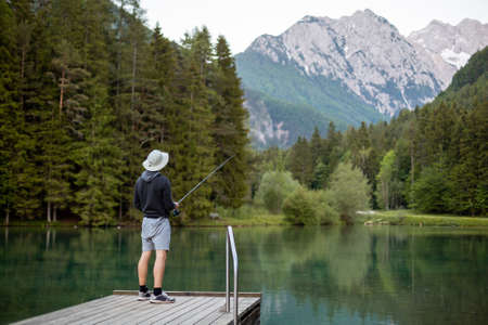 Man fishing on the pier in a beautiful lake and forest with mountains.の写真素材