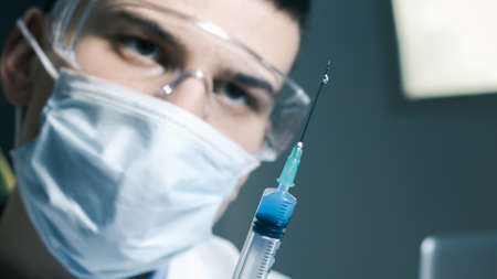 Doctor with syringe is preparing for vaccine injection and looking at needle, close-up.の写真素材