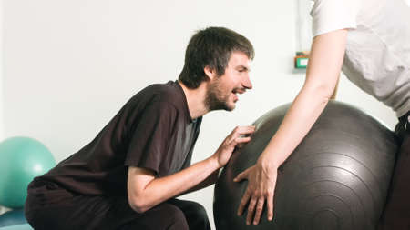 Physiotherapist exercising with disabled person on a therapy table using a ball.の写真素材