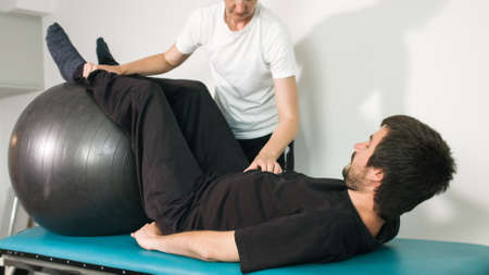 Physiotherapist exercising with disabled person on a therapy table using a ball.の写真素材