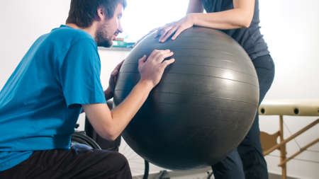 Physiotherapist exercising with disabled person on a therapy table using a ball.の写真素材