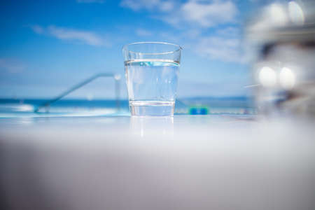 Glass of water standing near swimming pool in hot summerの写真素材