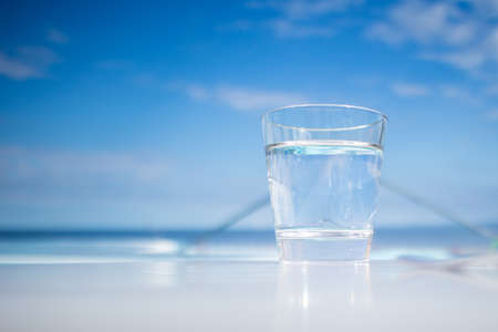 Glass of water standing near swimming pool in hot summer