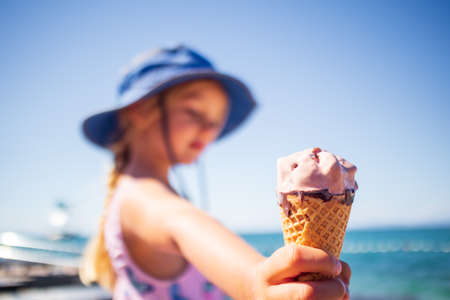 Happy girl child eating icecream in summer on a beach outdoors.