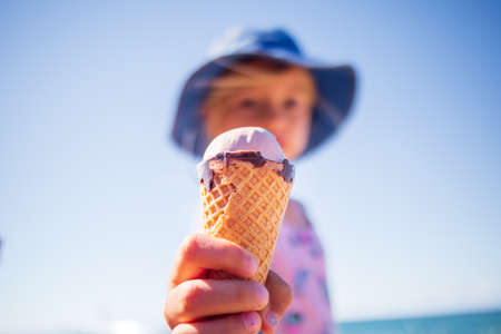Happy girl child eating icecream in summer on a beach outdoors.の写真素材