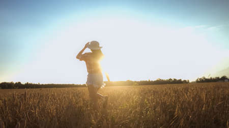 Beautiful girl in a throwing hat on a wheat field background. Warm summer time.の写真素材