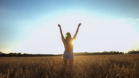Happy woman walking on a wheat field with open arms at the bright sun.の写真素材