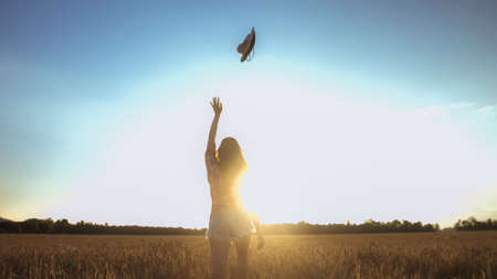 Beautiful girl in a throwing hat on a wheat field background. Warm summer time.の写真素材