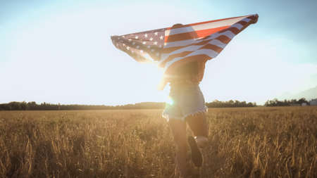 Young happy American girl running and jumping on 4th of July carefree with open arms over wheat...