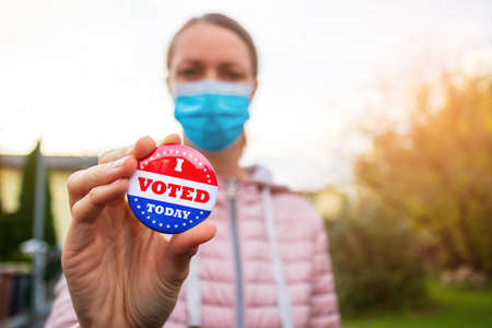 Woman with face mask showing I voted today button at american elections outside.の写真素材