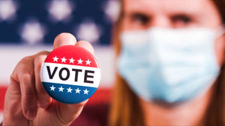 Woman with face mask showing Vote button with american flag. Extreme close-upの写真素材