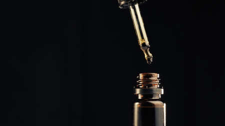 Bottle of Cbd cannabis oil against black background. Hand holding droplet.の写真素材